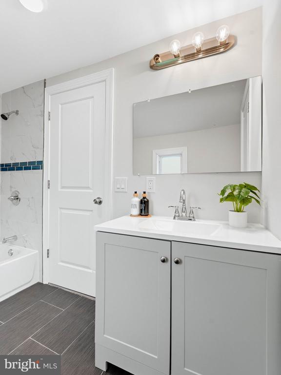 Bathroom with gray vanity, large mirror, and marble-look tub surround.