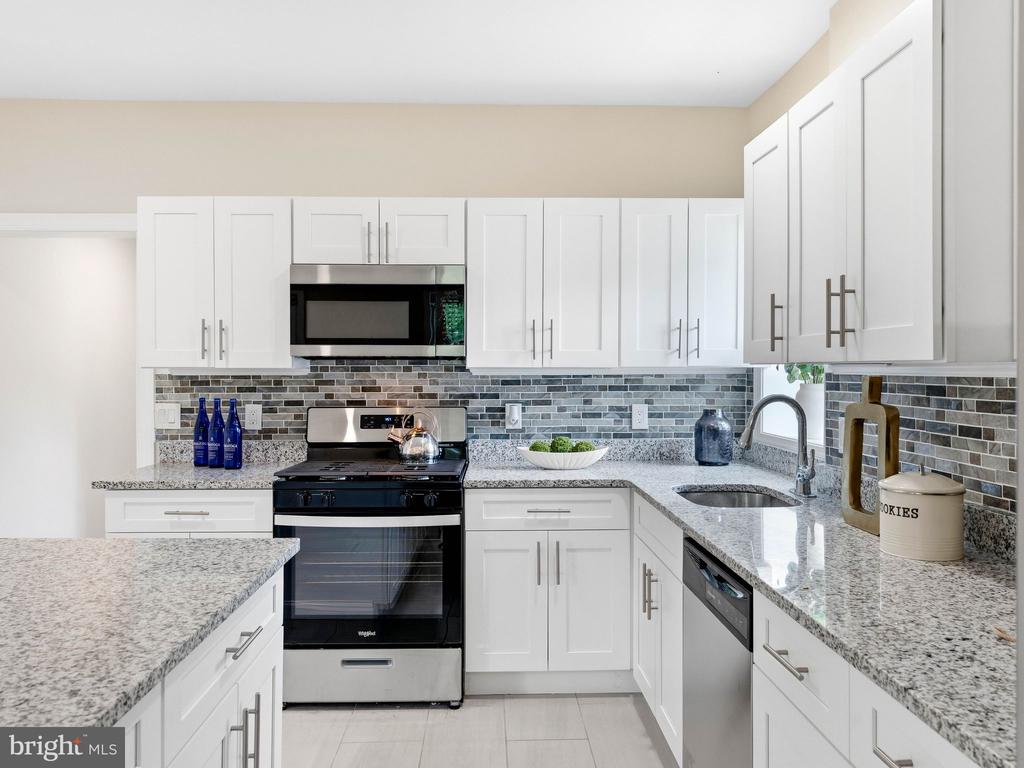 Modern kitchen with white shaker cabinets, gray granite counters, and a gray tile backsplash.