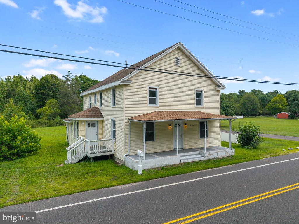 Two-story beige house with a covered front porch beside a road.