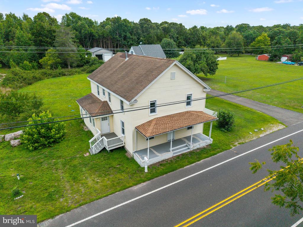 Aerial view of a two-story house beside a road, with a covered porch and broad grassy lot.