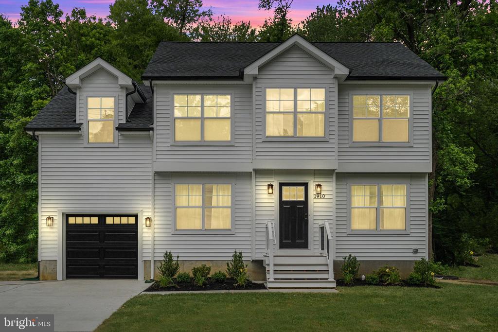 Two-story gray house with a black garage door and illuminated windows at dusk.