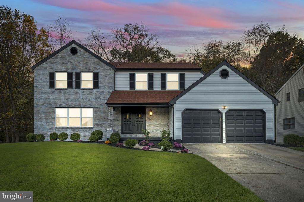 Two-story stone-and-siding home with a double garage and landscaped front lawn at dusk.
