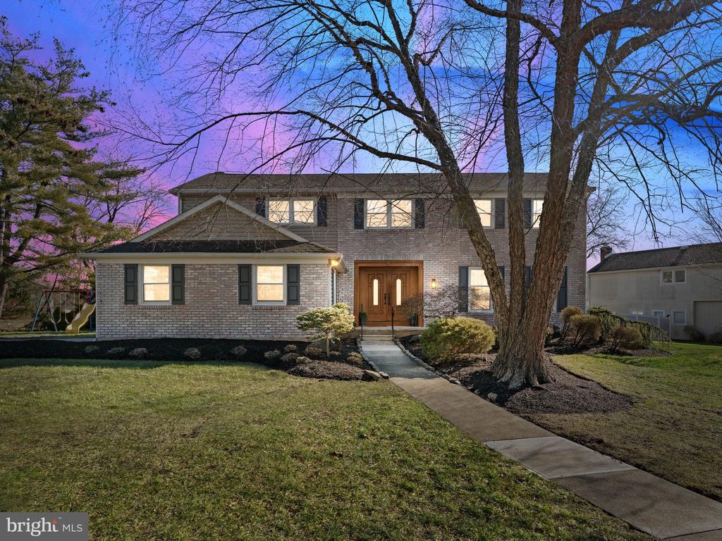 Two-story brick house with illuminated windows, double entry doors, and a walkway through the front lawn.