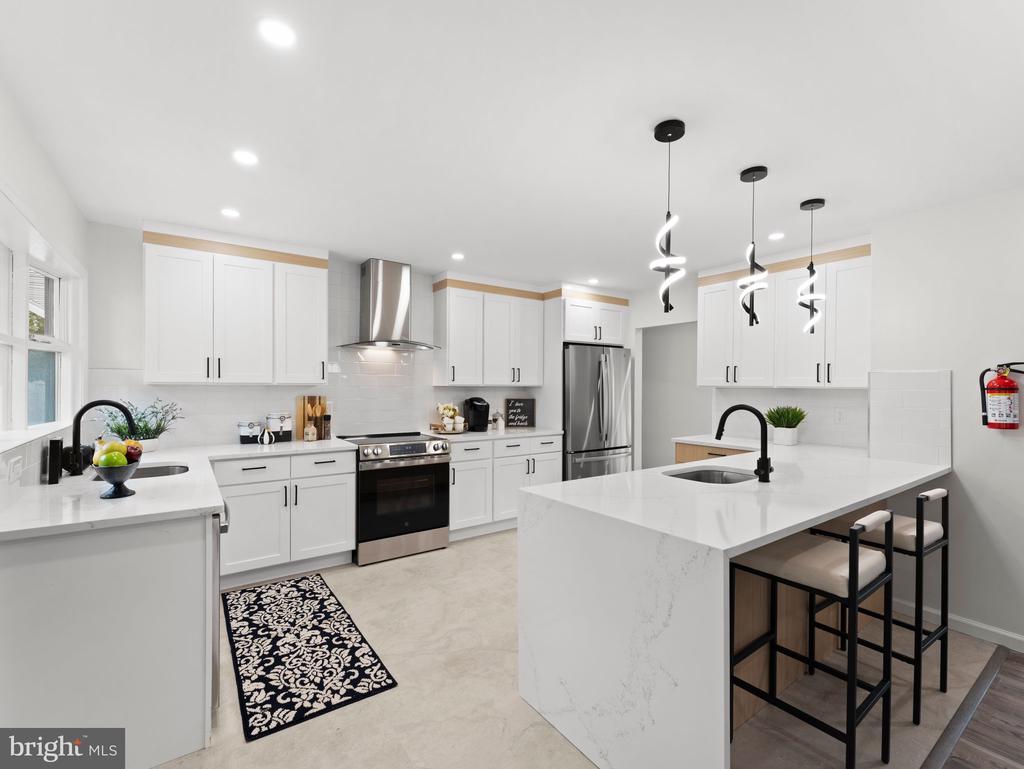 Bright white kitchen with stainless steel appliances, a large island, and sculptural pendant lights.