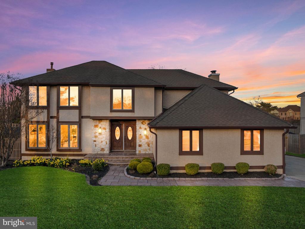 Two-story stucco home with stone accents and illuminated windows at dusk.