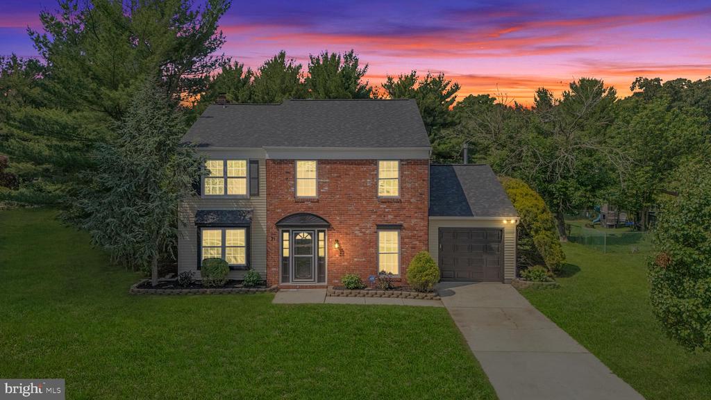Two-story brick home with an attached garage and illuminated windows at dusk.