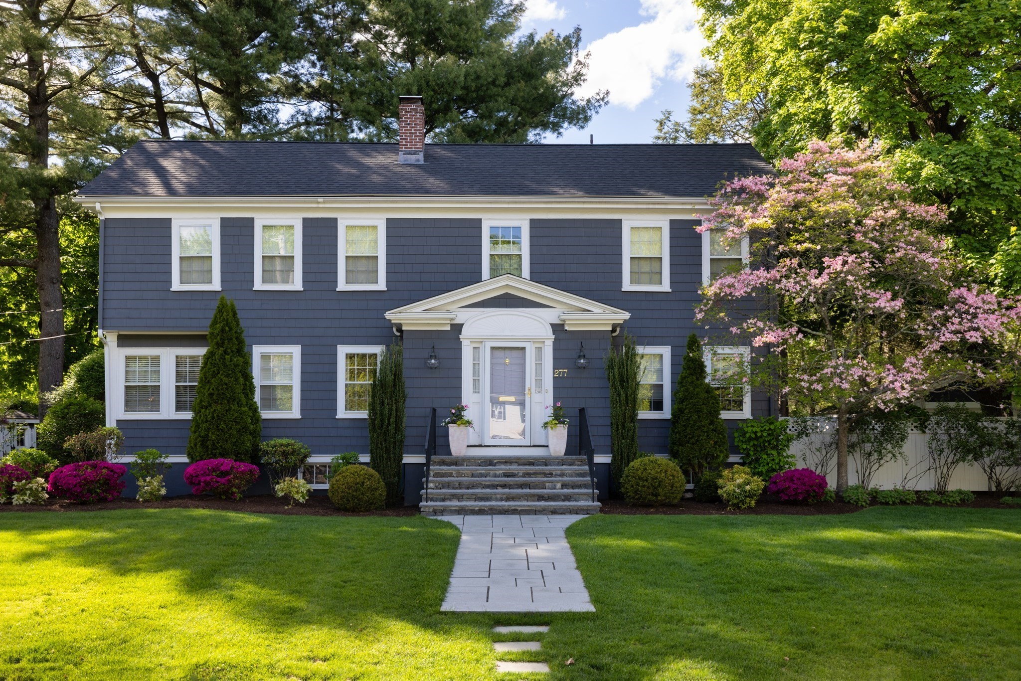 Slate-blue two-story house with white trim, a central pedimented entrance, and a landscaped front lawn.