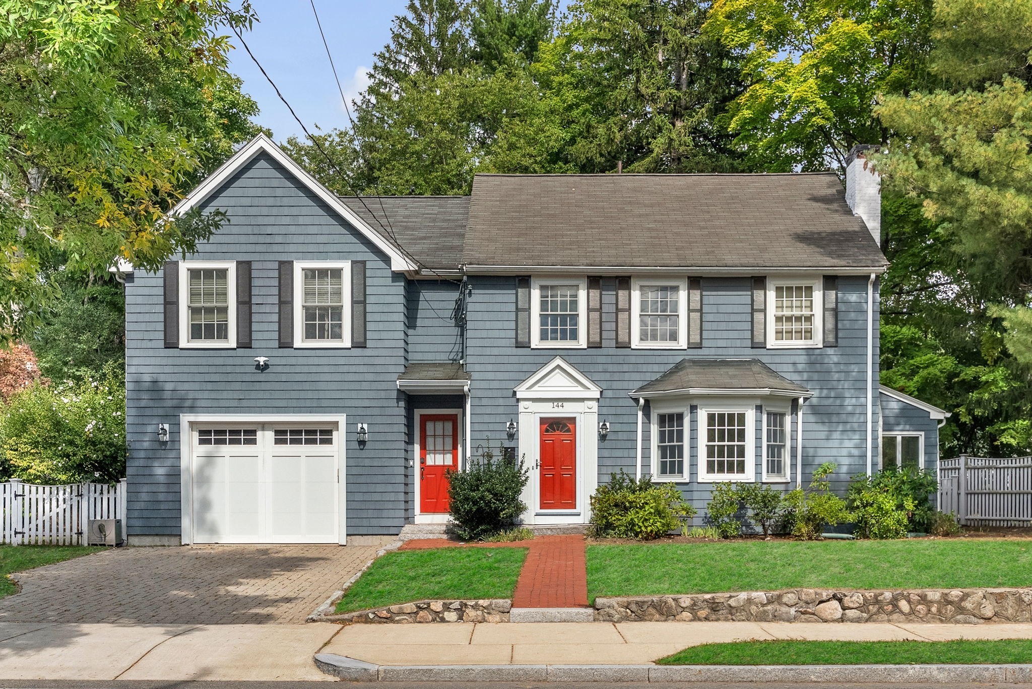 Blue-gray two-story house with red doors, an attached garage, and a landscaped lawn.