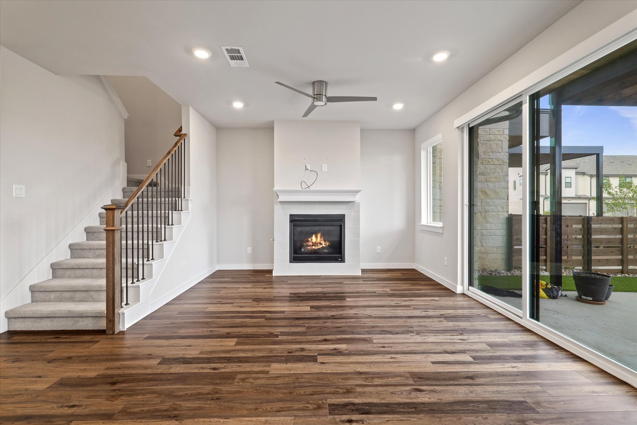 Vacant living room with a tiled fireplace, staircase, and sliding glass doors to a patio.