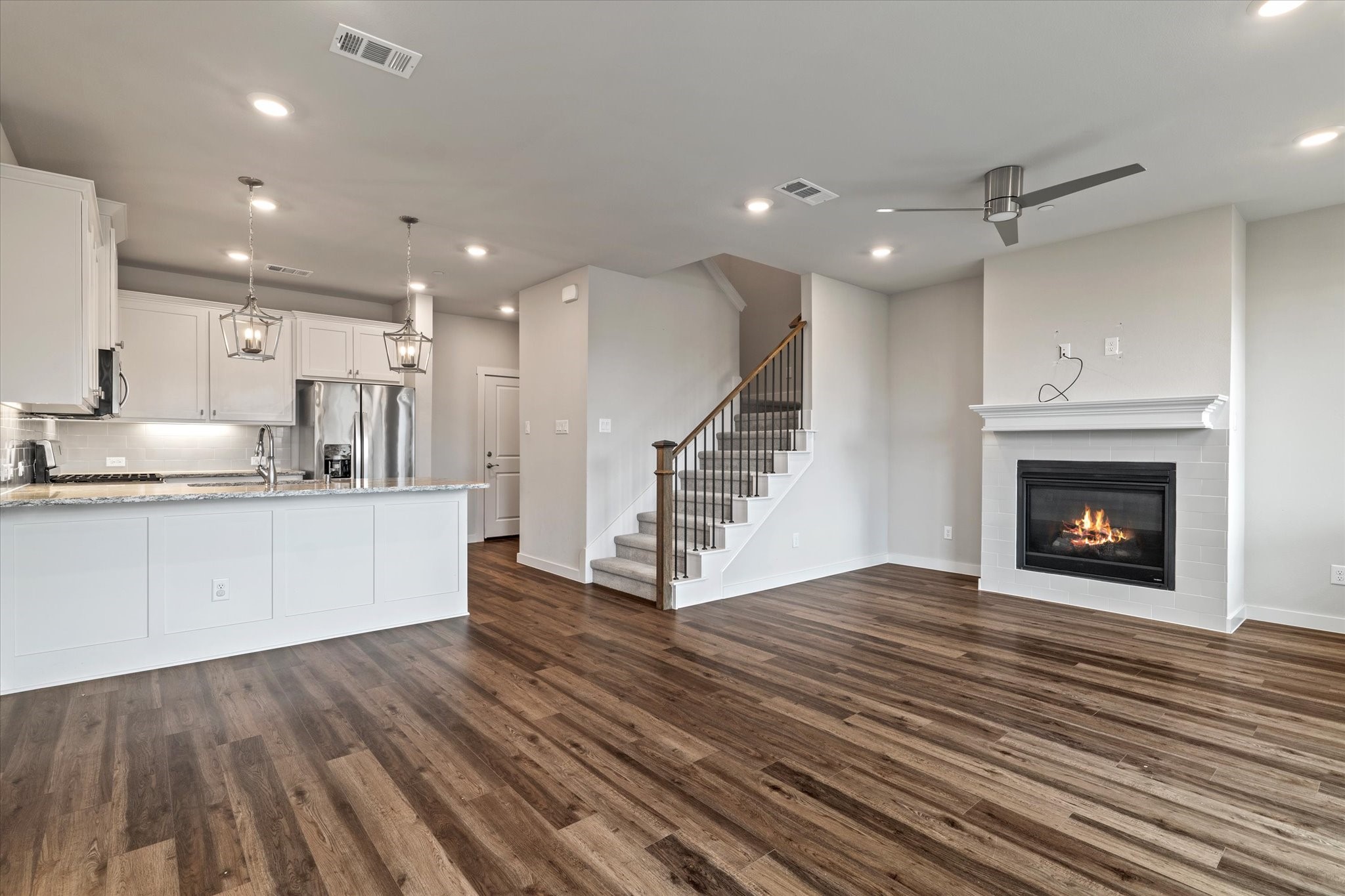 Unfurnished open-plan kitchen and living area with dark wood floors and a lit fireplace.