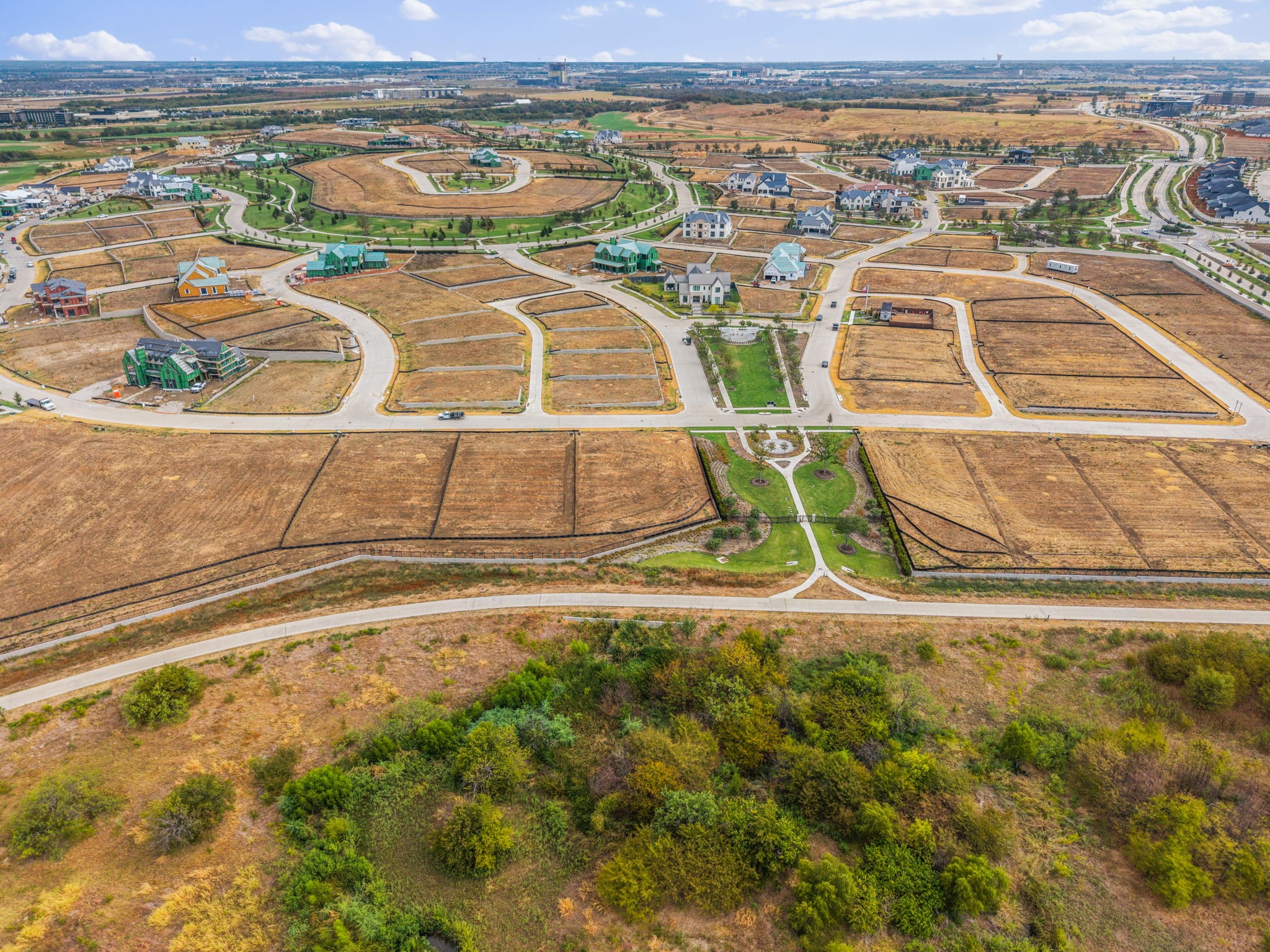 Aerial view of vacant subdivision lots, curving streets, scattered homes, and a landscaped park.