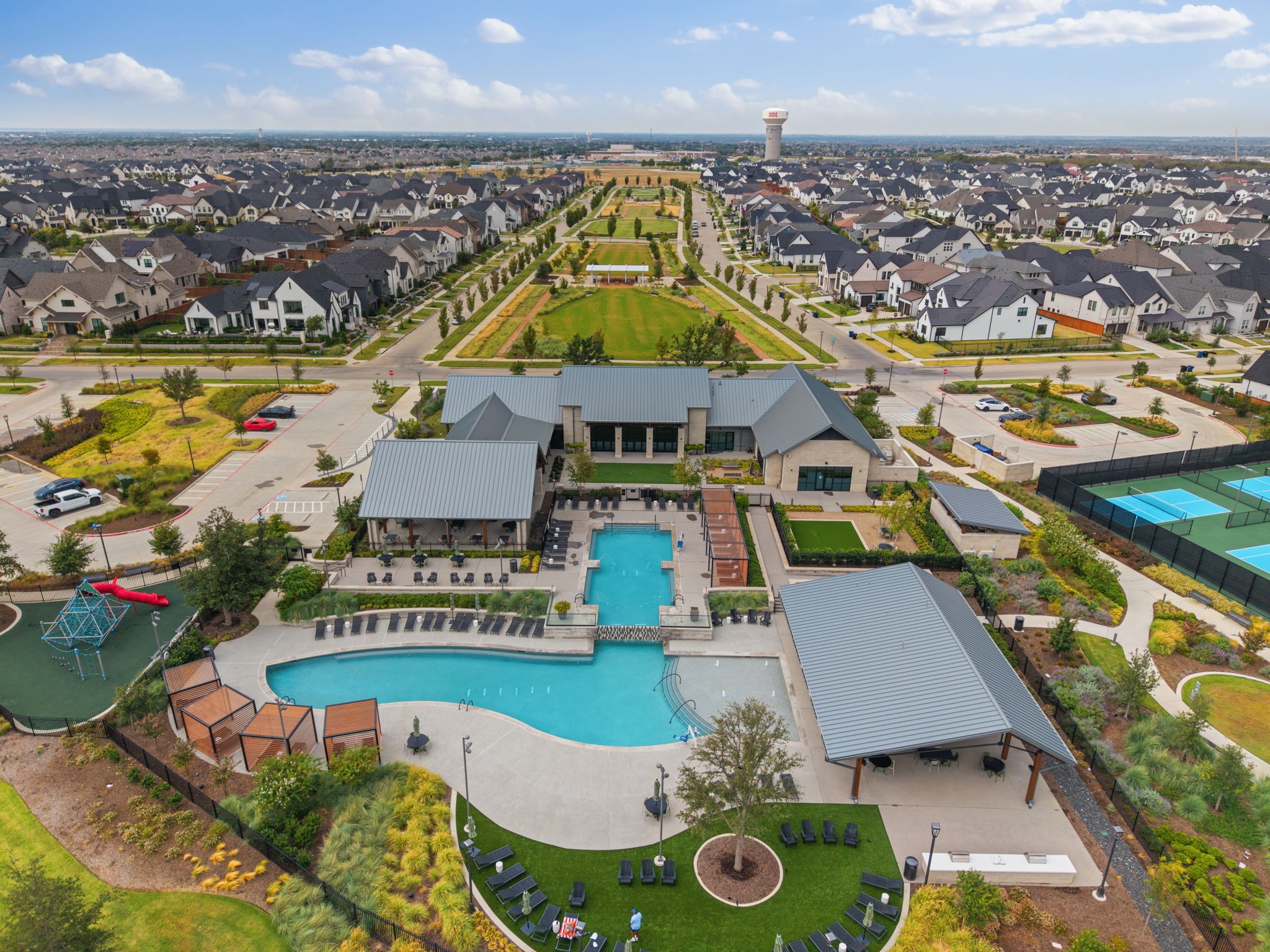 Aerial view of neighborhood clubhouse and pools, with pickleball courts, playground, and landscaped grounds.