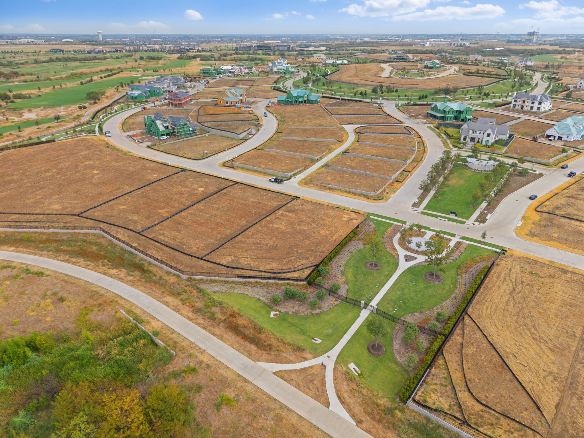 Aerial view of vacant residential lots, winding streets, and a landscaped neighborhood park.