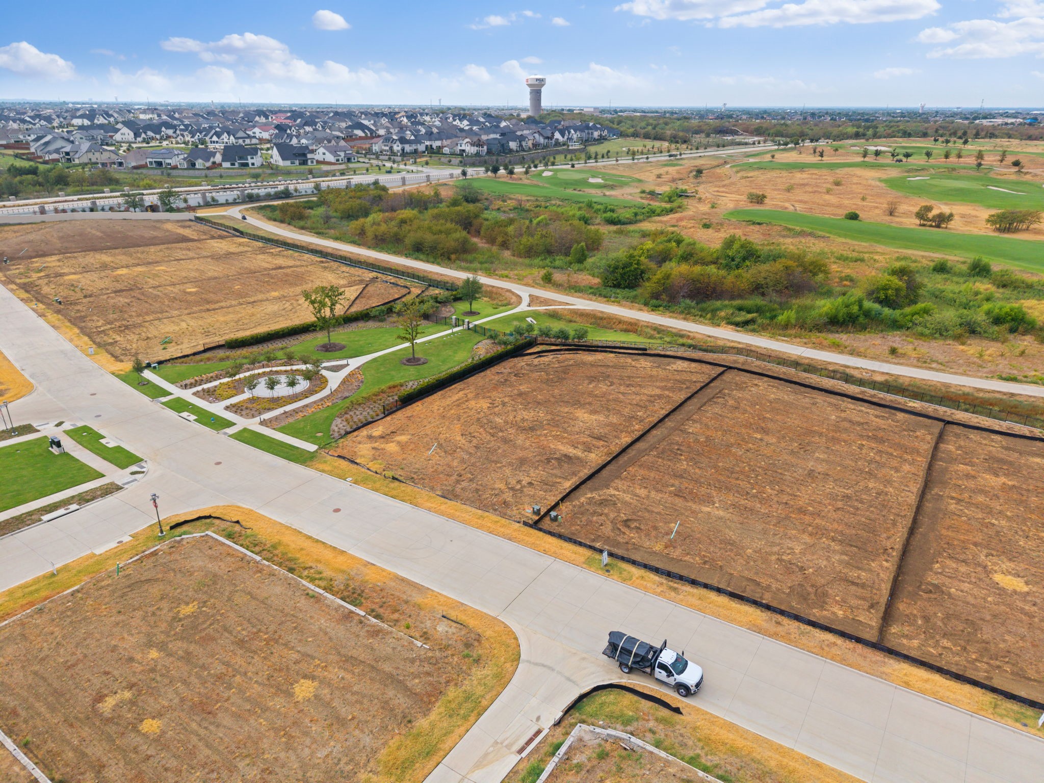 Aerial view of vacant building lots beside a landscaped path and golf course.