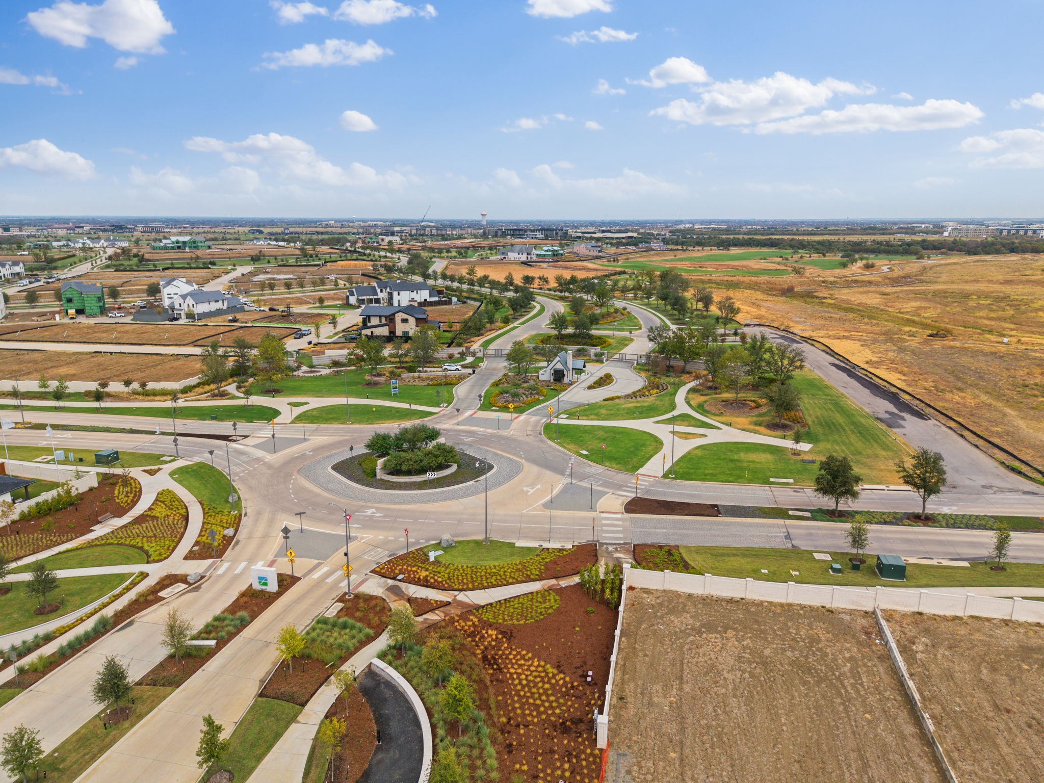 Aerial view of a landscaped neighborhood roundabout, curving streets, new homes, and open development lots.