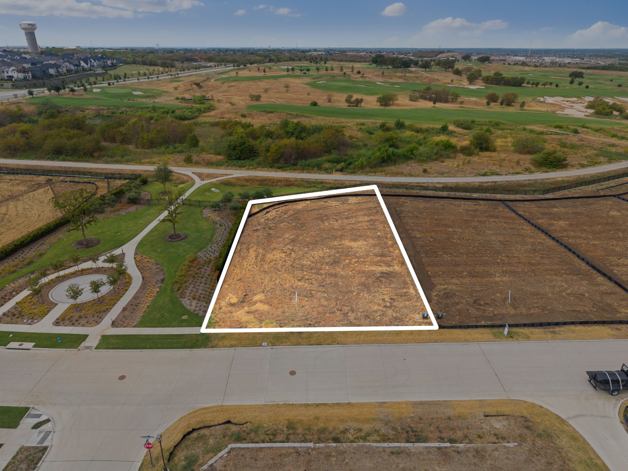 Aerial view of a vacant lot outlined in white beside a street, with a golf course and walking path behind it.