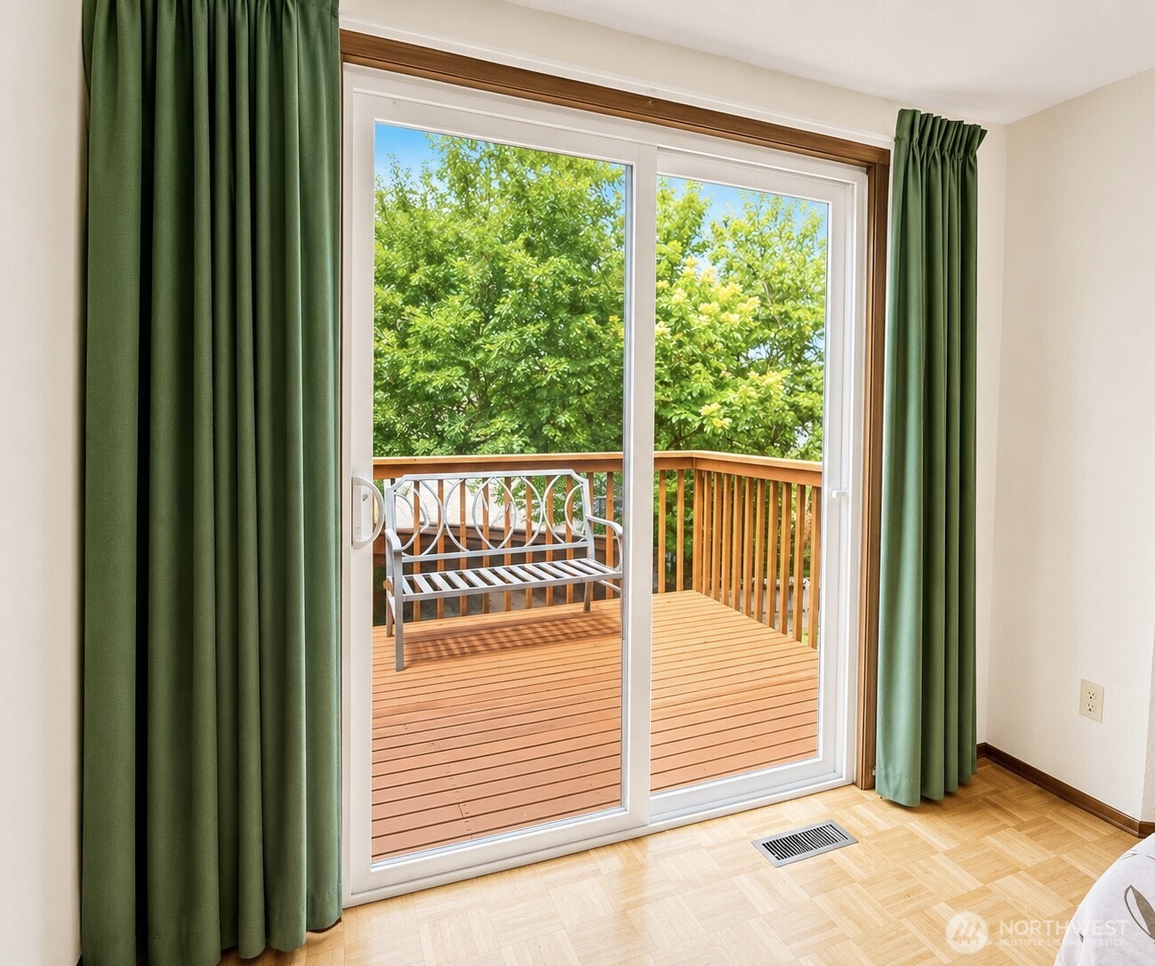 Bedroom with green curtains and parquet flooring opening onto a wooden deck with a metal bench.