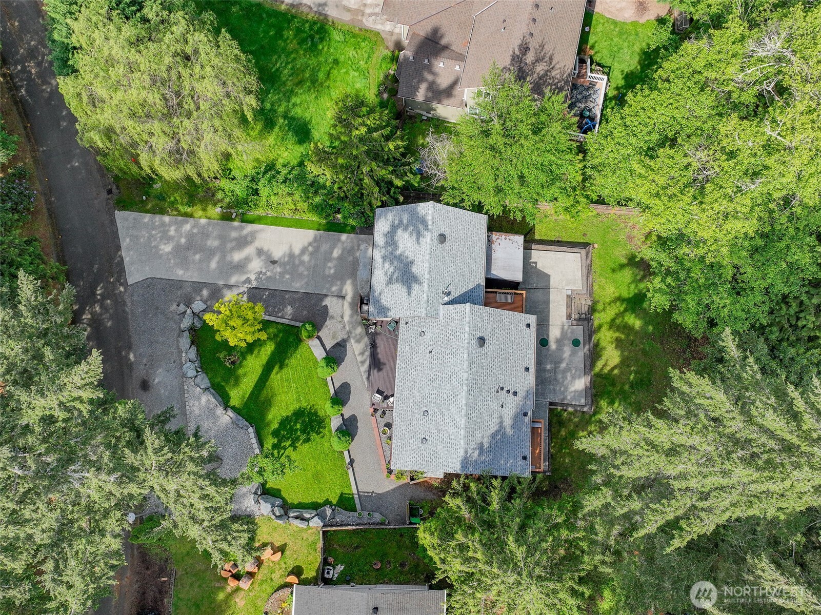 Aerial view of a house surrounded by trees, with a landscaped lawn and curving driveway.