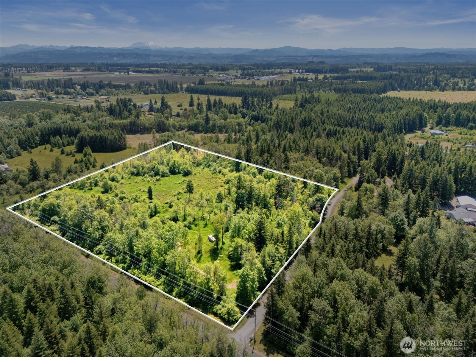 Aerial view of a wooded parcel outlined in white, with forest and distant mountains.