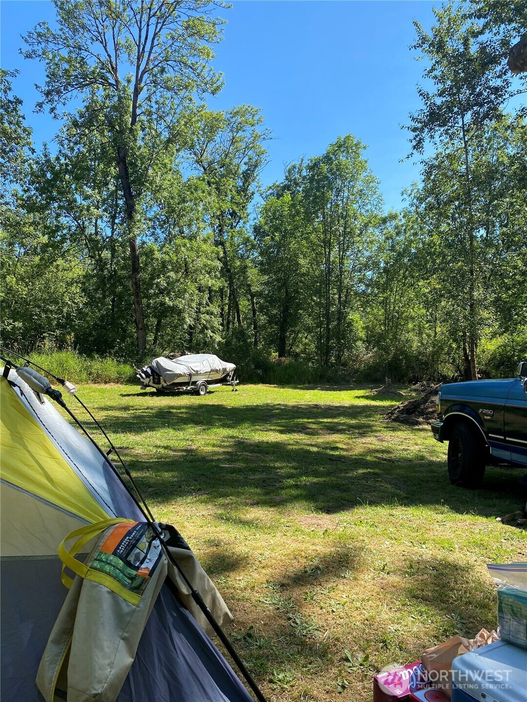 Wooded property clearing with camping tent and covered boat on a trailer.