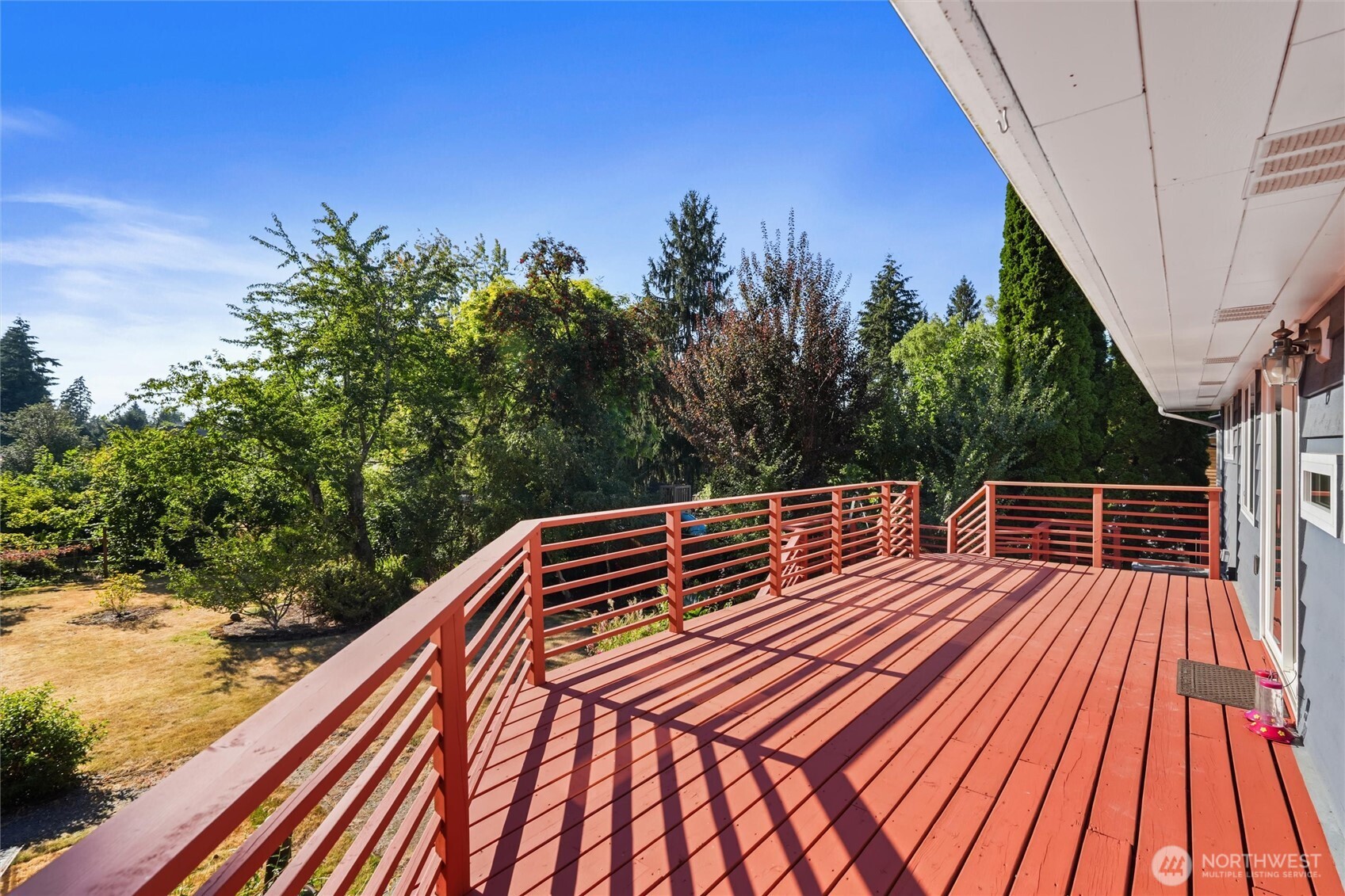 Red deck beside the house overlooking a tree-filled yard.