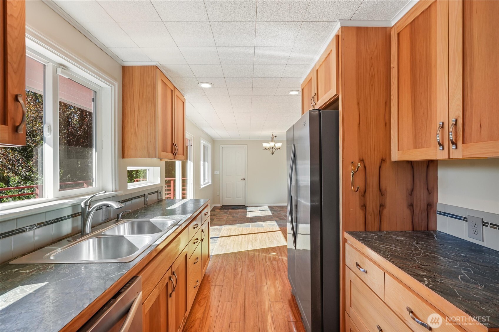 Kitchen with warm wood cabinets, dark countertops, a double sink, and stainless-steel refrigerator.