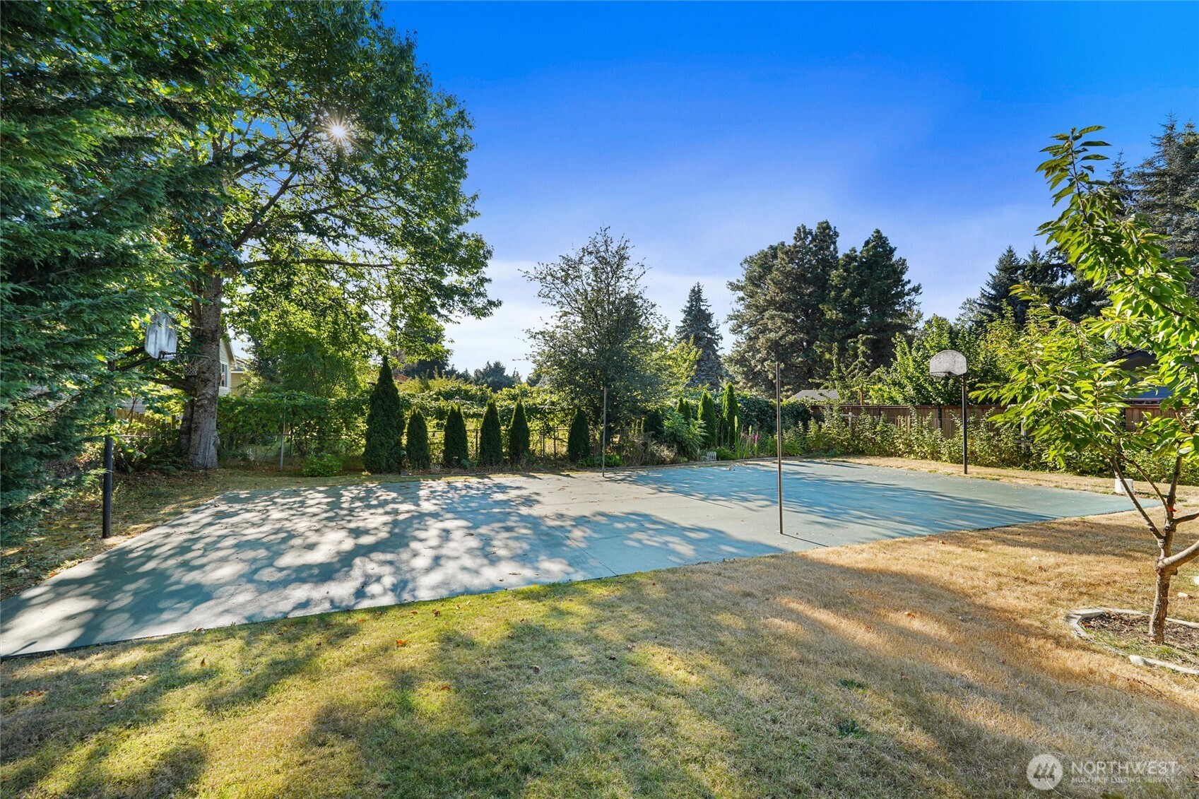 Backyard basketball court with two hoops, mature trees, and a fenced perimeter.