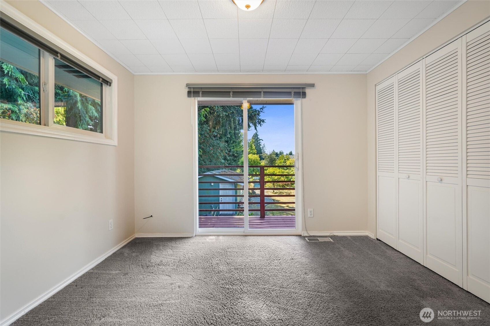 Empty carpeted bedroom with louvered closets and a sliding glass door to a balcony.