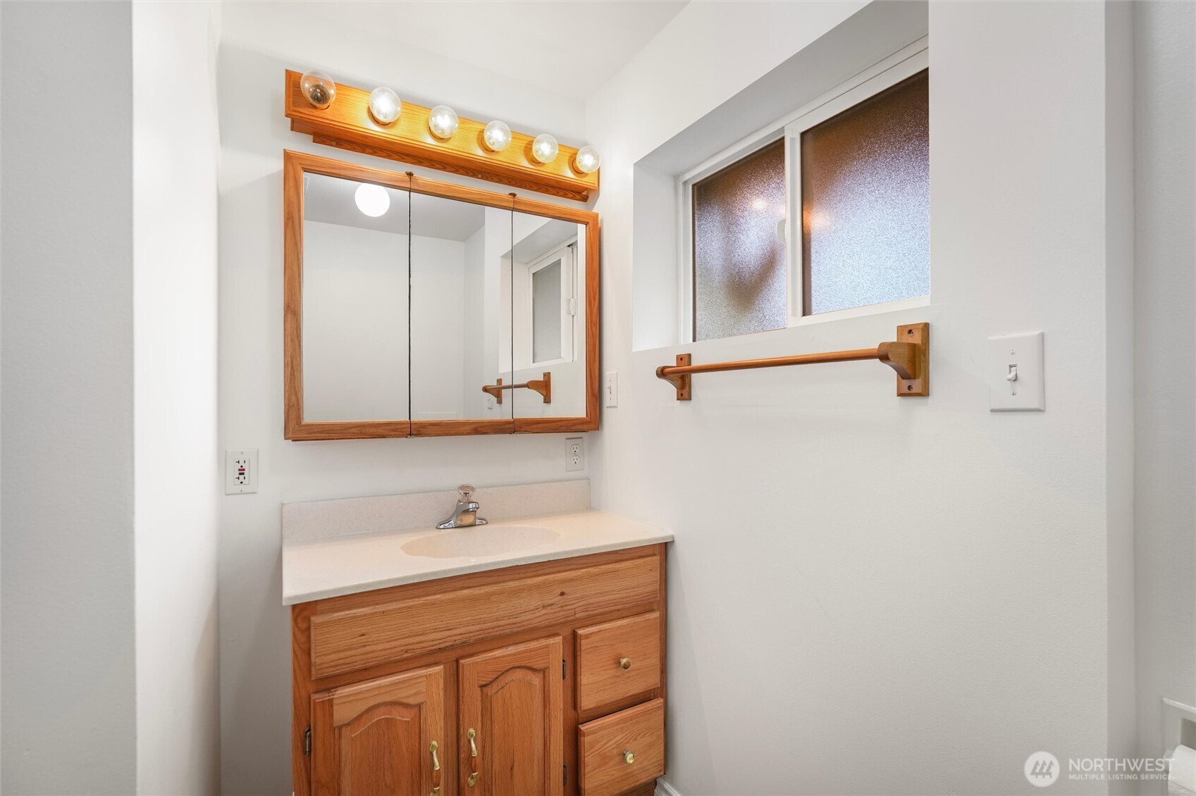 Bathroom vanity with a wood cabinet, mirrored medicine cabinet, globe lights, and wooden towel bar.