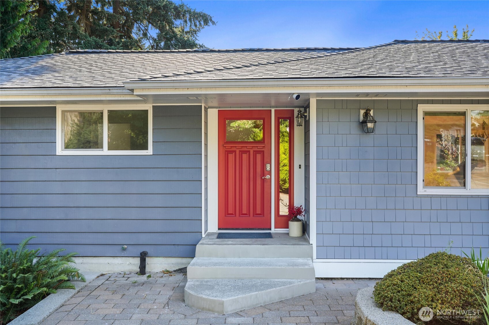 Home entrance with a bright red front door, narrow glass sidelight, and concrete steps.