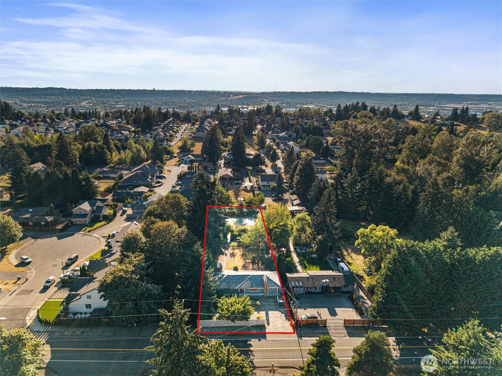 Aerial view of a house and tree-filled lot outlined in red, with a pool behind the home.