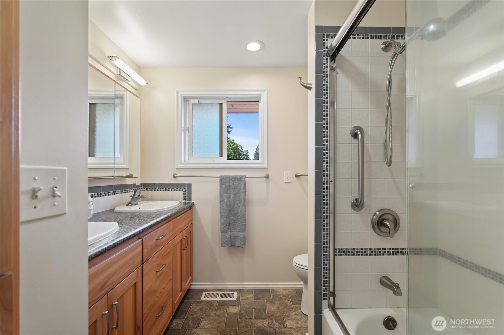 Bathroom with a glass-enclosed tub and shower beside a double-sink wood vanity.