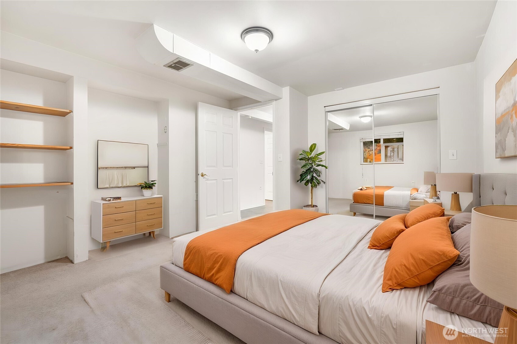 Staged bedroom with orange-and-white bedding, mirrored closet doors, and built-in wooden shelves.