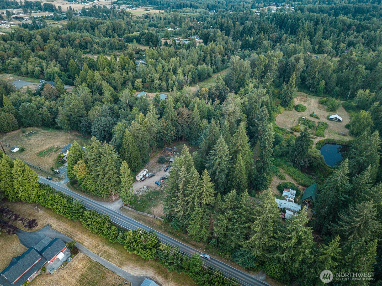 Wooded property with a pond, clearing, scattered outbuildings, and road frontage.