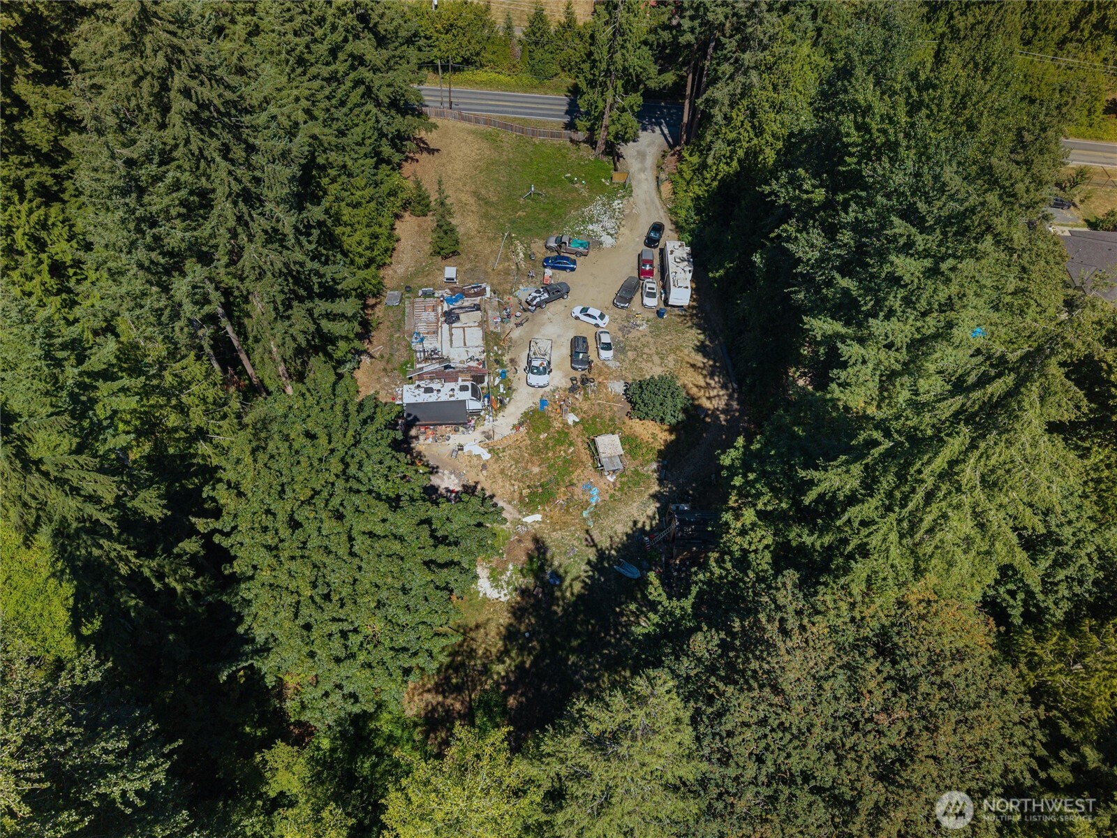 Aerial view of a wooded lot with a clearing, parked vehicles, trailers, and building materials.