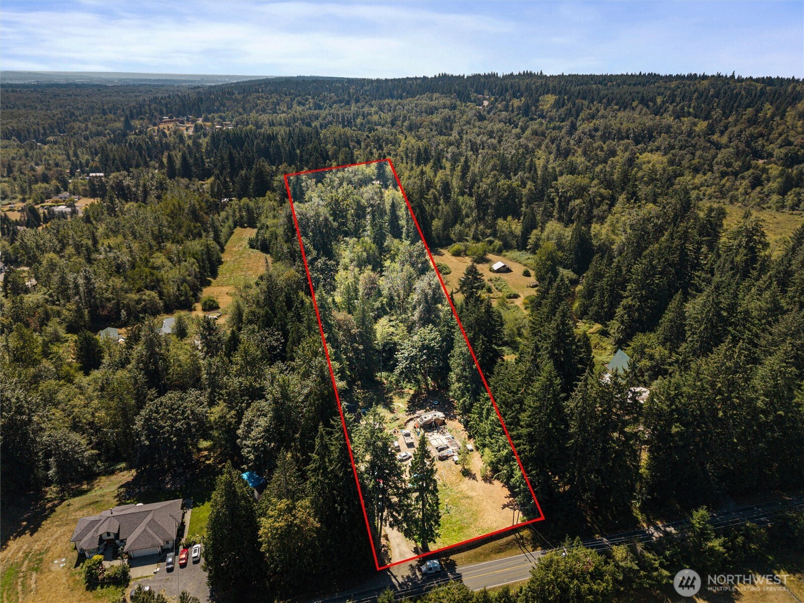 Aerial view of a wooded property outlined in red, with a clearing and road frontage.