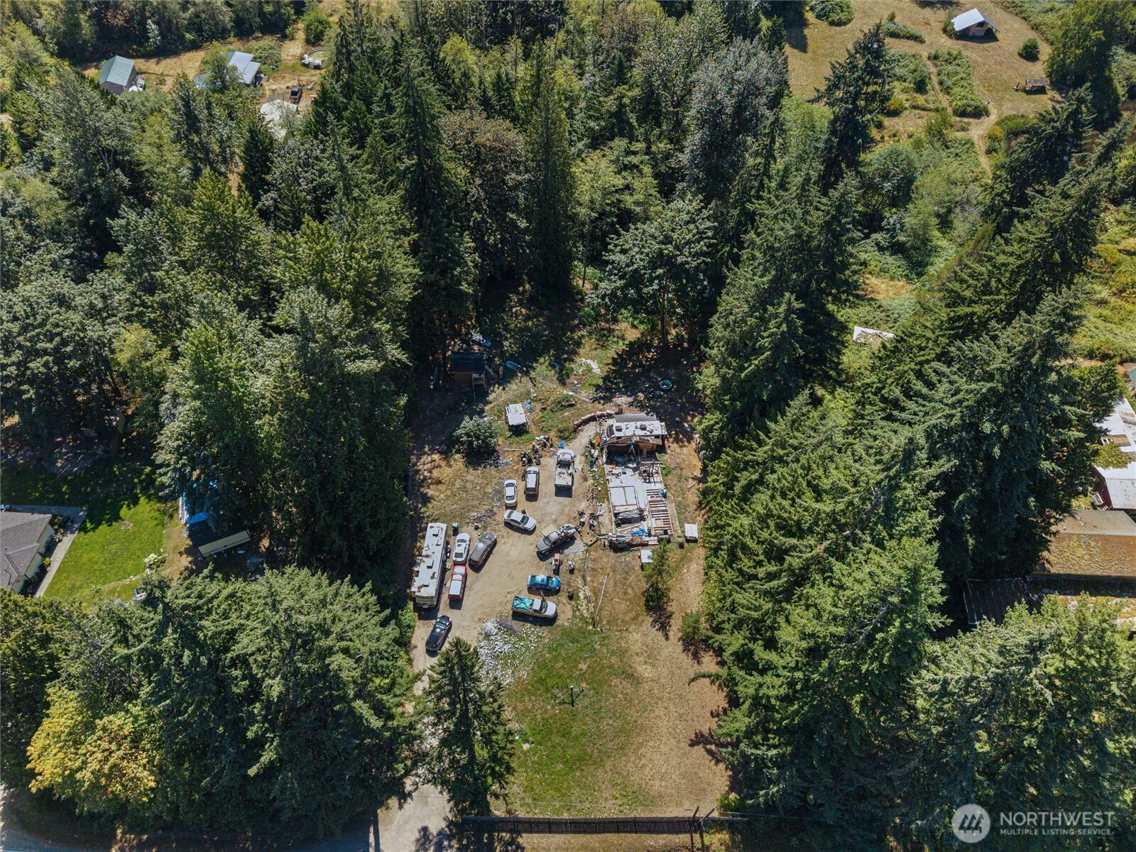 Aerial view of a wooded property with a clearing, vehicles, RVs, and scattered structures.