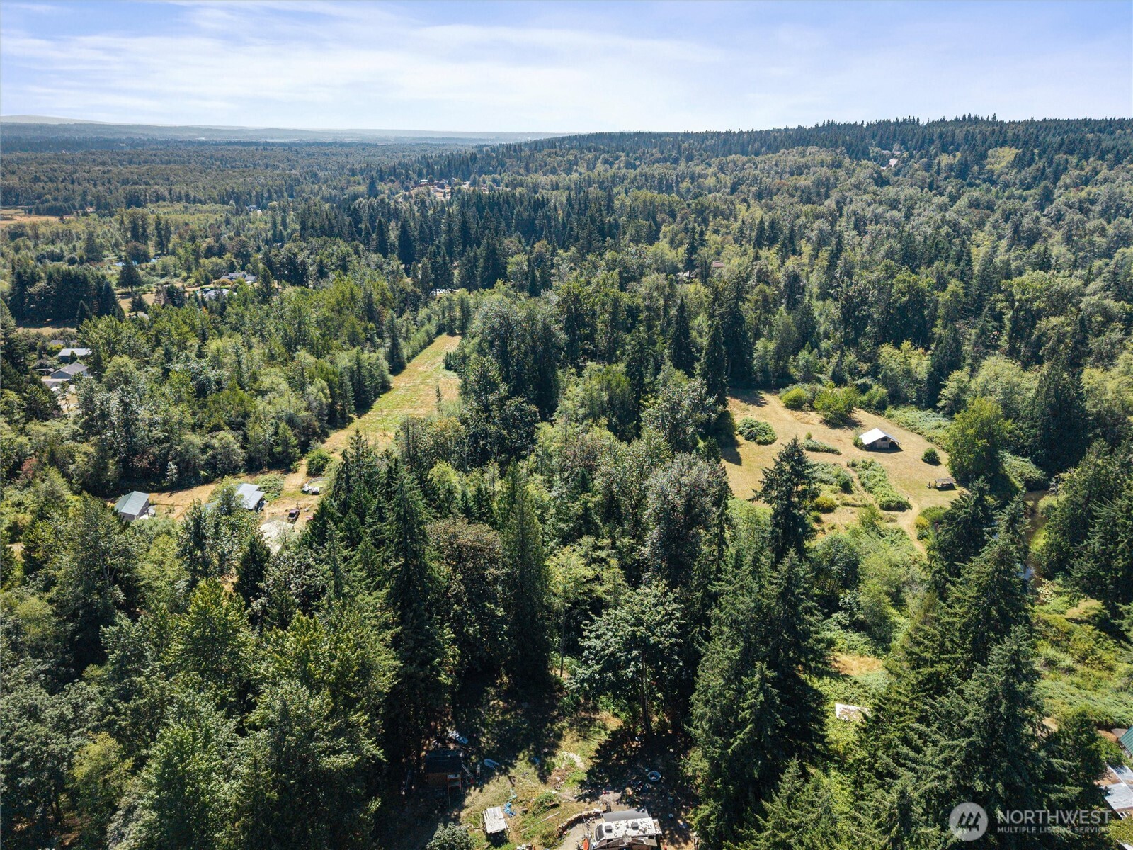 Aerial view of wooded acreage with grassy clearings and scattered small structures.