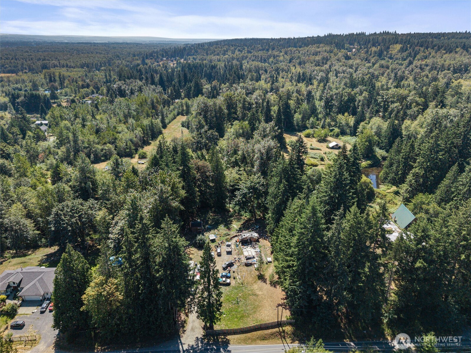 Aerial view of a wooded property with a construction site in a clearing beside the road.