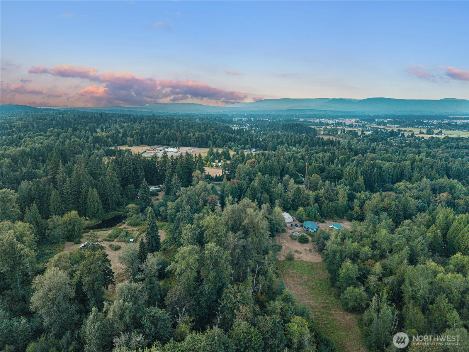 Aerial view of wooded rural property with open clearings, scattered homes, and distant mountain ridges.