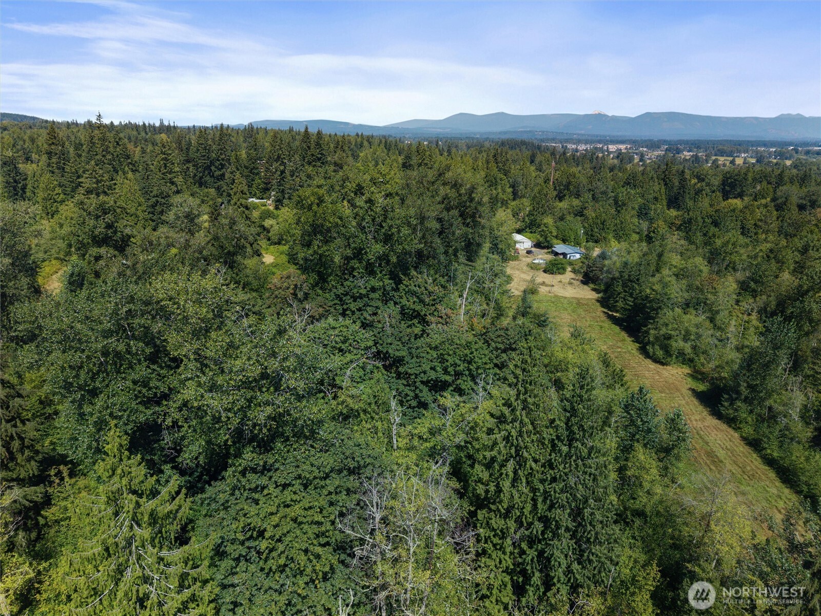 Aerial view of a forested property with a grassy clearing and distant mountain ridges.