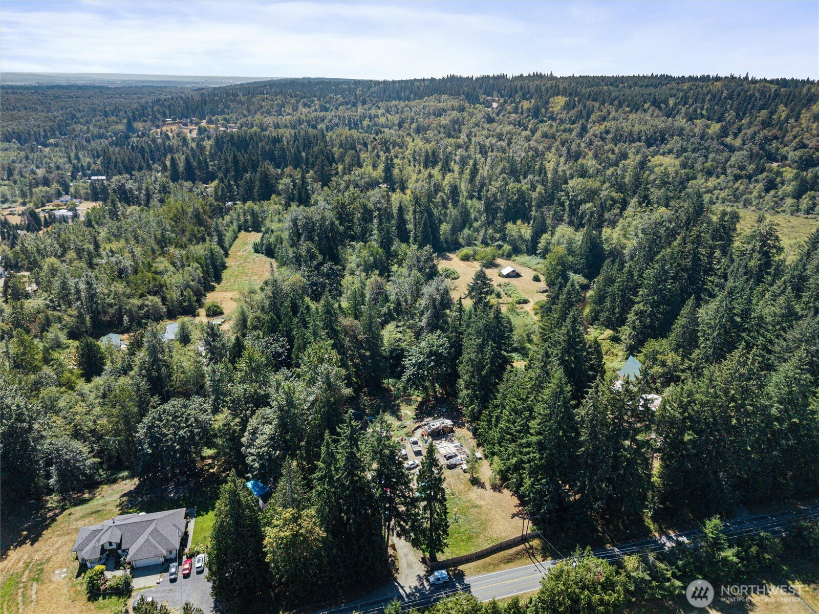 Aerial view of a wooded property with open clearings, scattered buildings, and a road along the edge.
