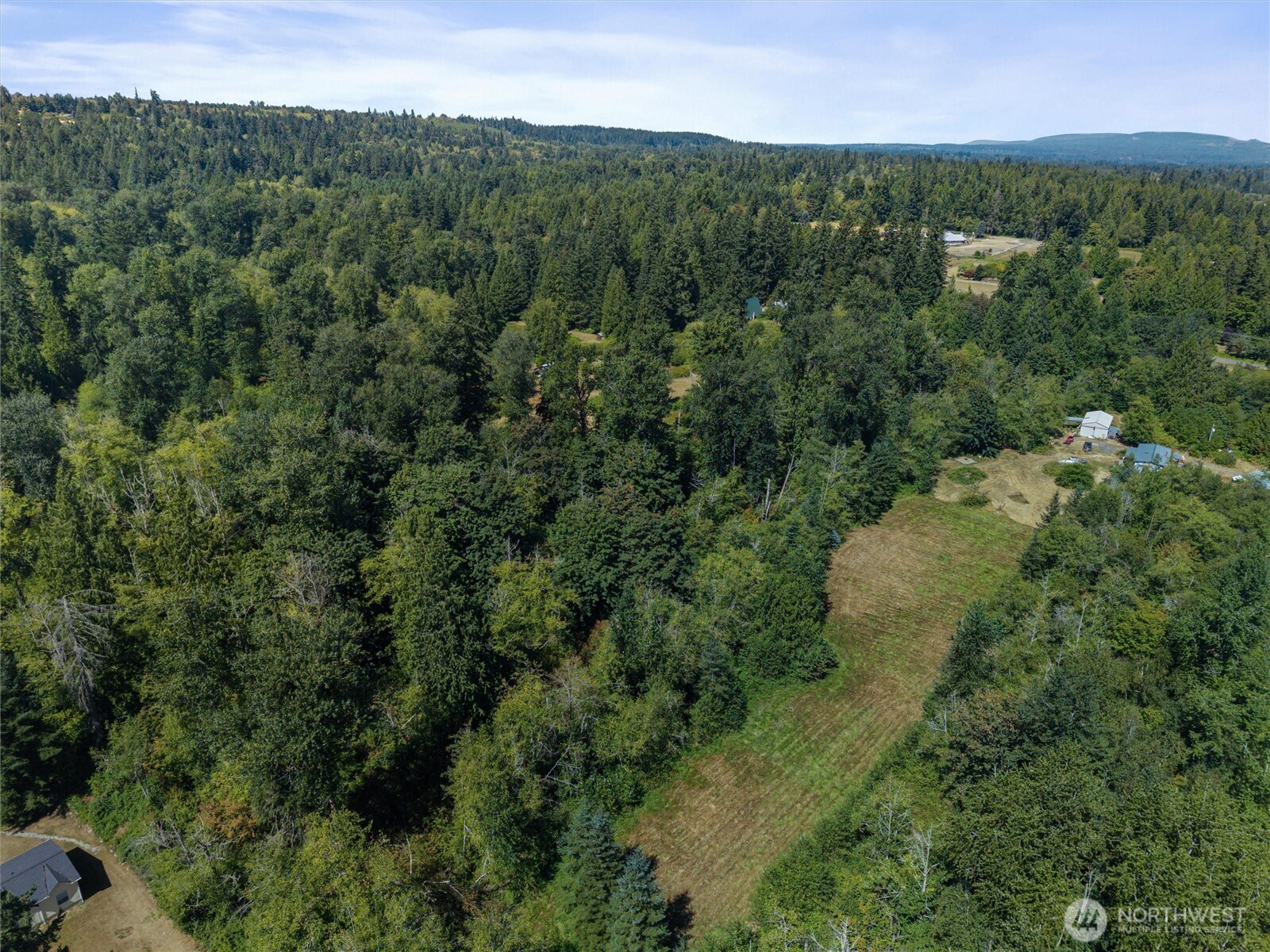 Aerial view of a wooded property with a long grassy clearing and forested hills beyond.