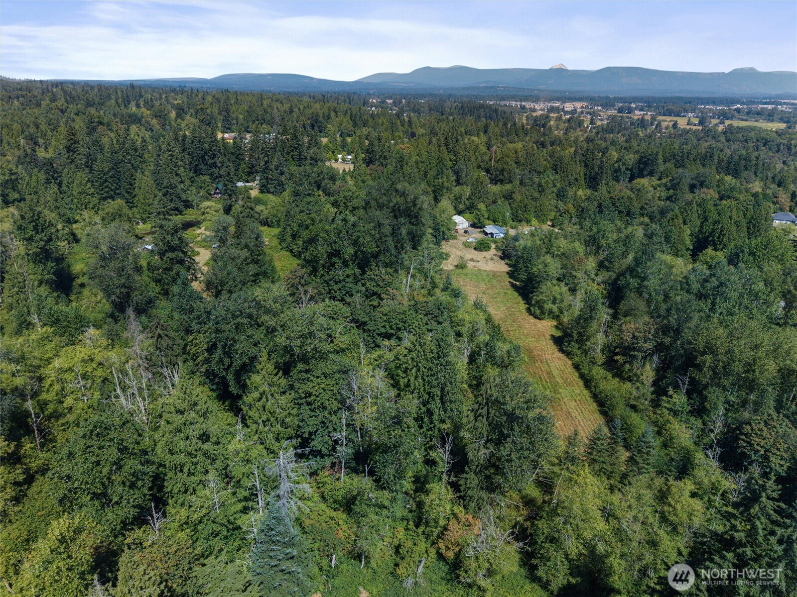 Aerial view of wooded acreage with a grassy clearing and distant mountain range.
