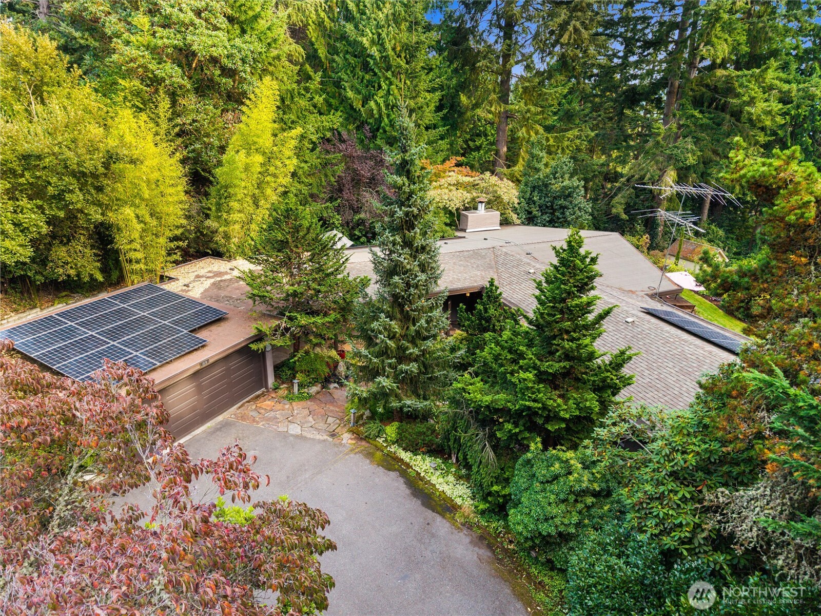 Aerial view of a wooded home with rooftop solar panels and an attached garage.