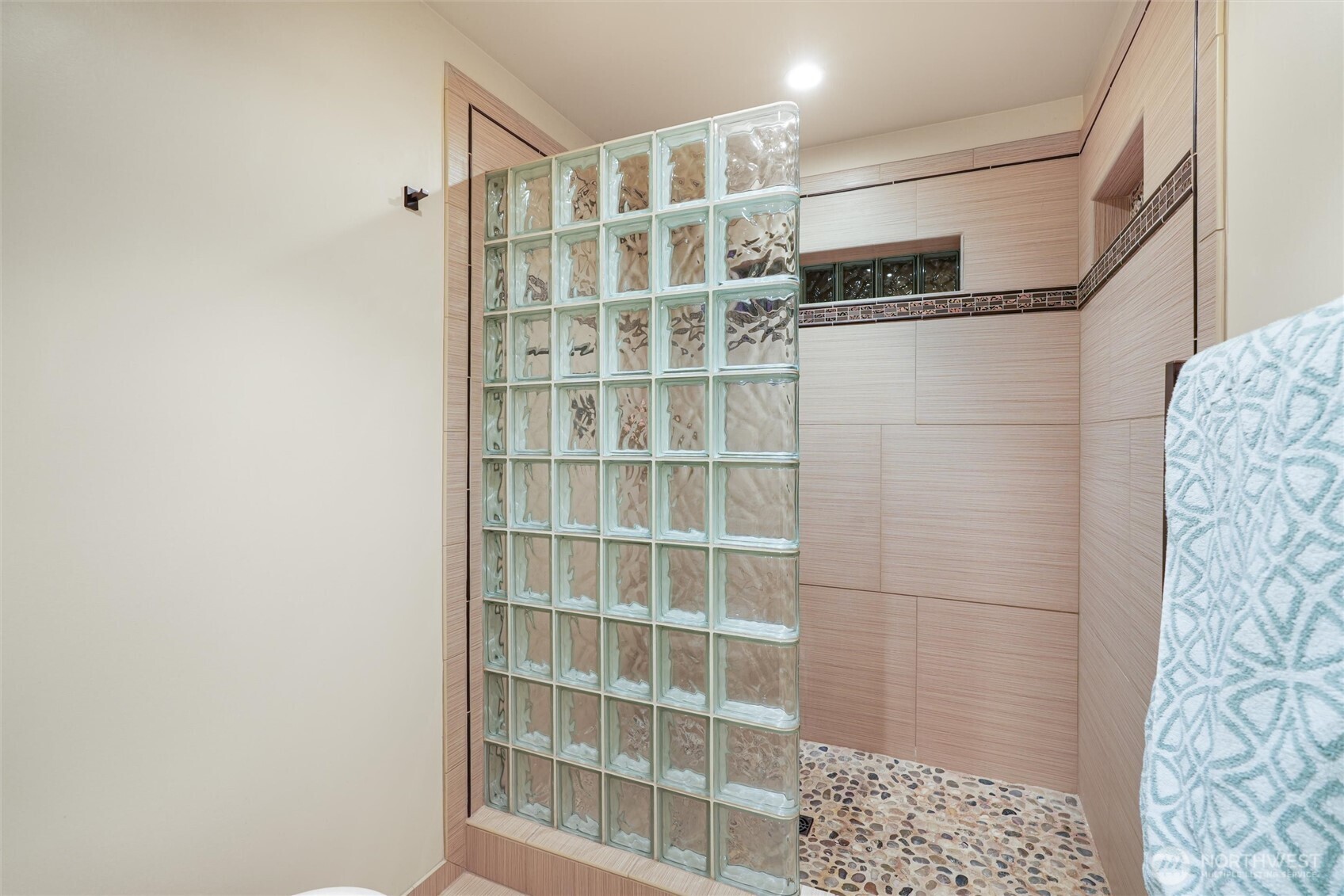 Bathroom shower with a glass-block partition, warm-toned tile, and pebble-stone floor.