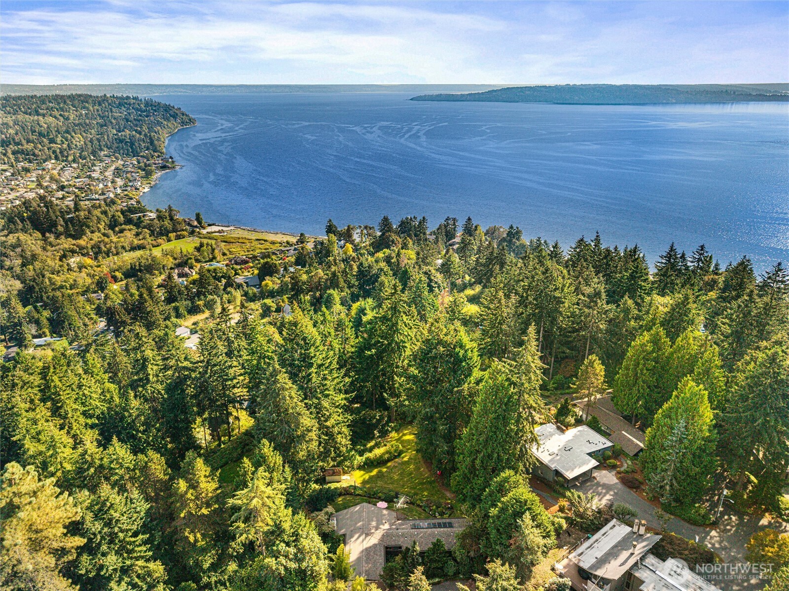 Aerial view of homes among trees overlooking a broad blue bay.