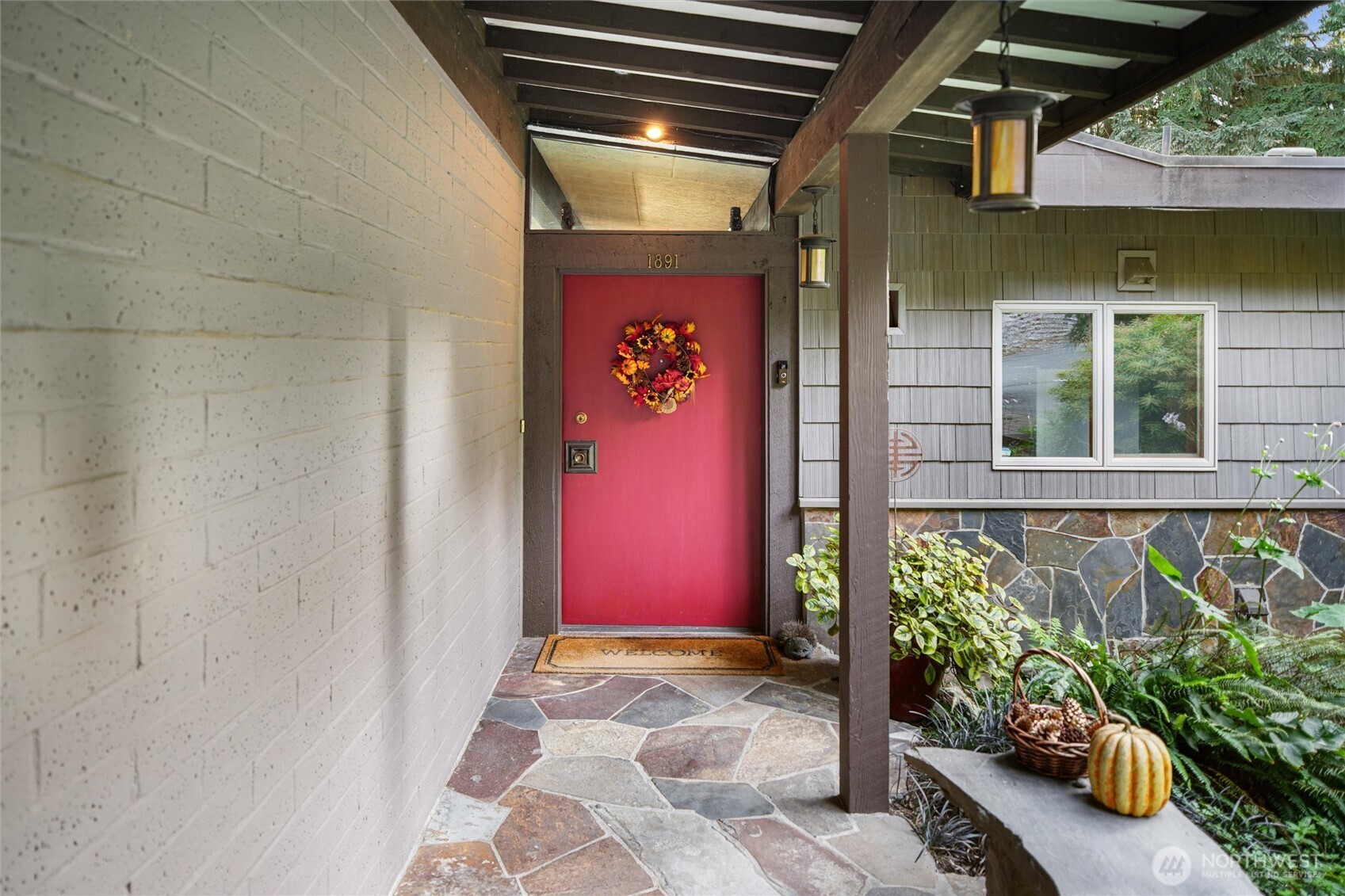 Covered home entry with a red wreath-decorated door, stone paving, and a pumpkin display.
