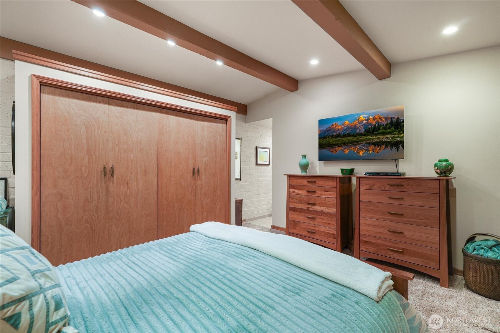Bedroom with a turquoise quilted bed, wood closet doors, and exposed ceiling beams.
