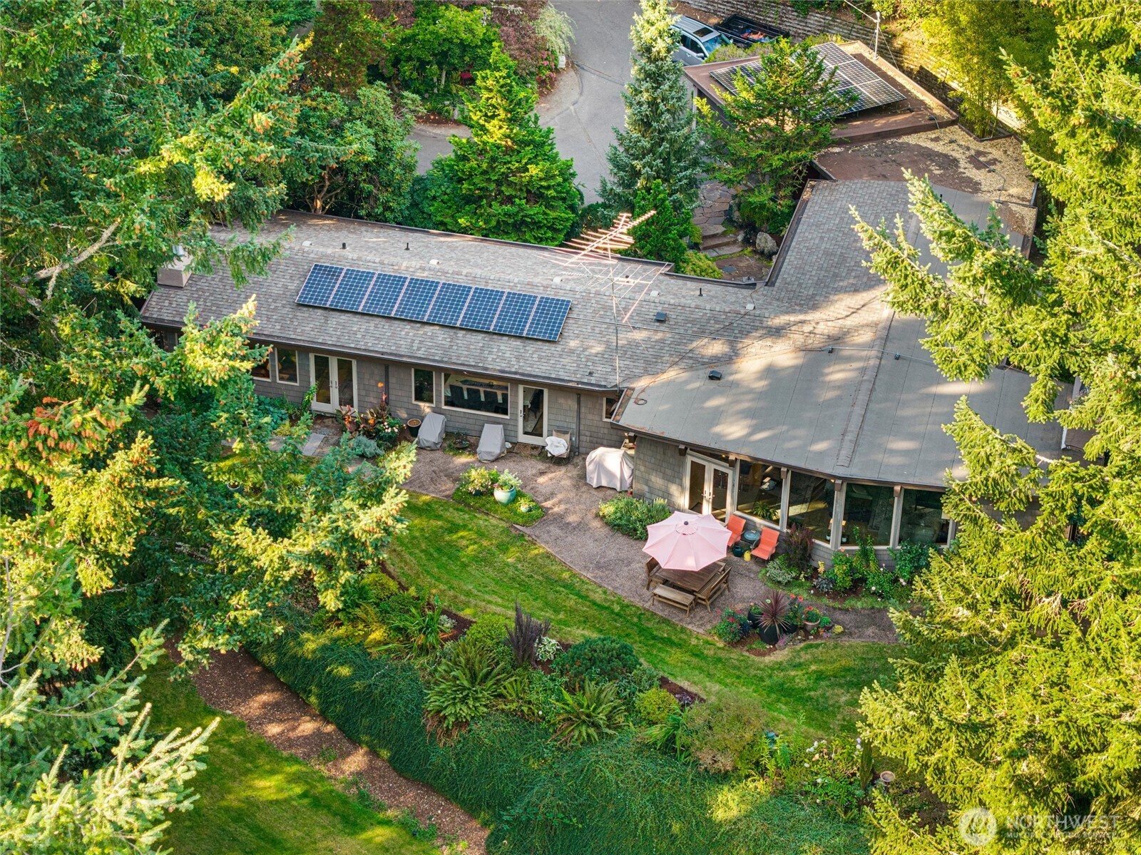 Aerial view of a tree-surrounded home with rooftop solar panels and a furnished garden patio.
